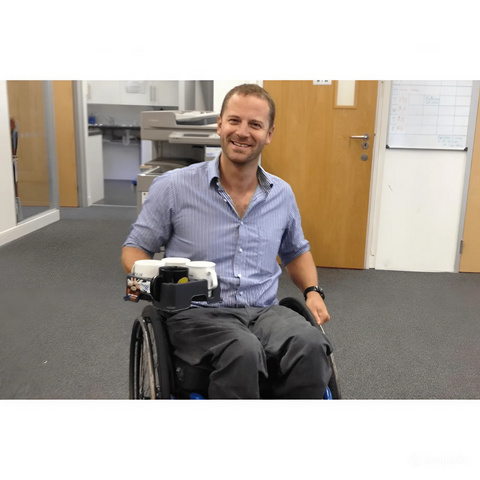 A person sitting in a wheelchair using the Muggi Cup Holder to transport drinks, showcasing its accessibility and convenience for wheelchair users.