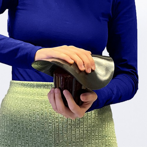 A woman is using the uccello grip mat in order to open the lid off a jar. This is desgined to give extra grip when twisting so that minimal effort and strength is required by the user, so they can maintain their independence with useful kitchen aids.